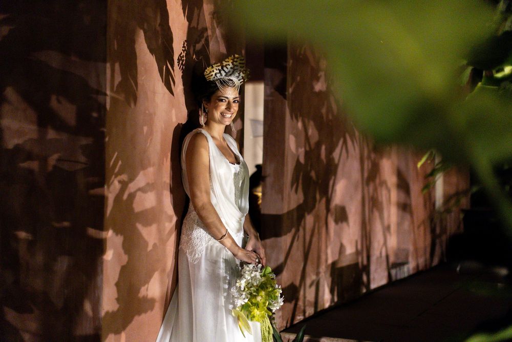 A person in a white wedding dress holds a yellow bouquet while standing against a wall with dramatic shadows.