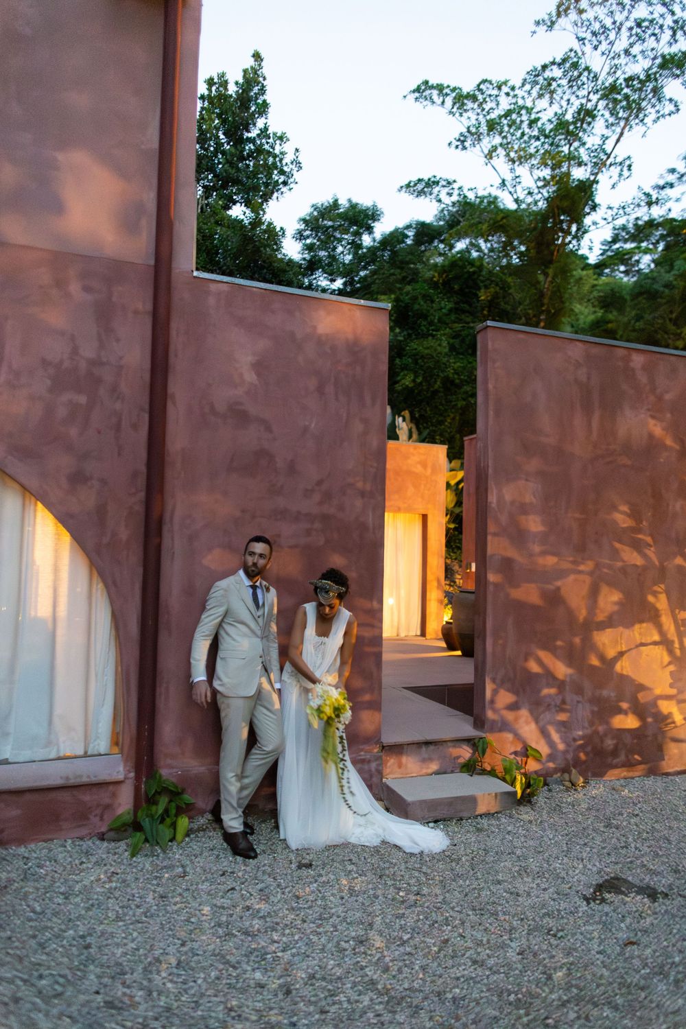 A wedding couple poses for artistic photos along a rustic wall with warm lighting at sunset.