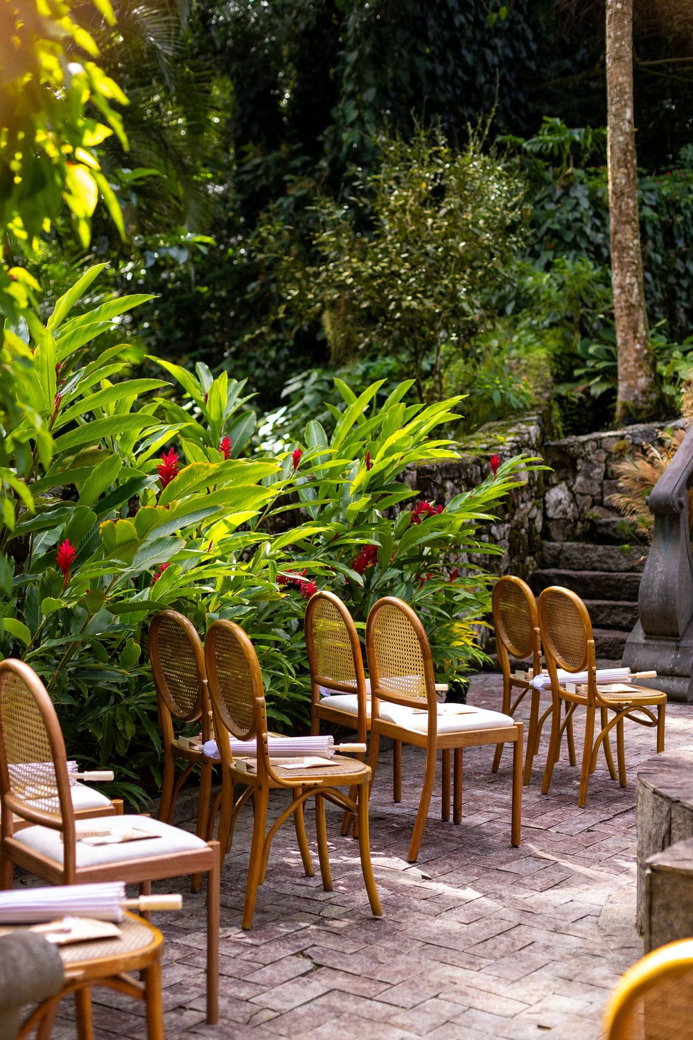 Outdoor restaurant patio with wicker chairs and lush tropical garden setting on stone paving.