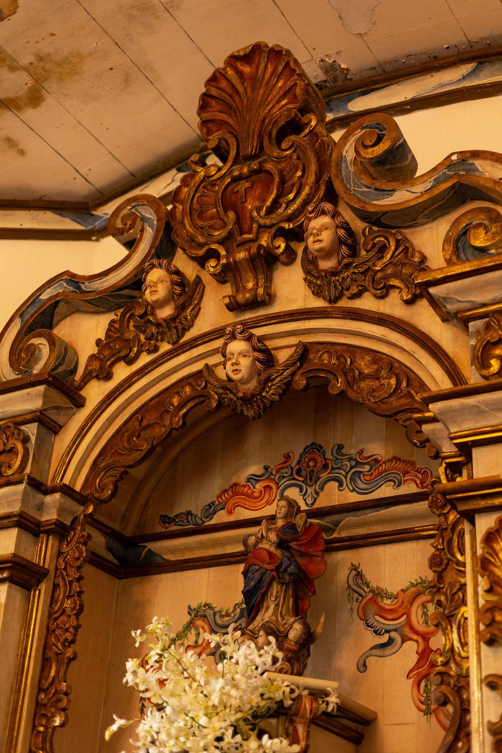 Ornate baroque-style wooden architectural details with intricate carvings and gilded decorative elements on a church ceiling.