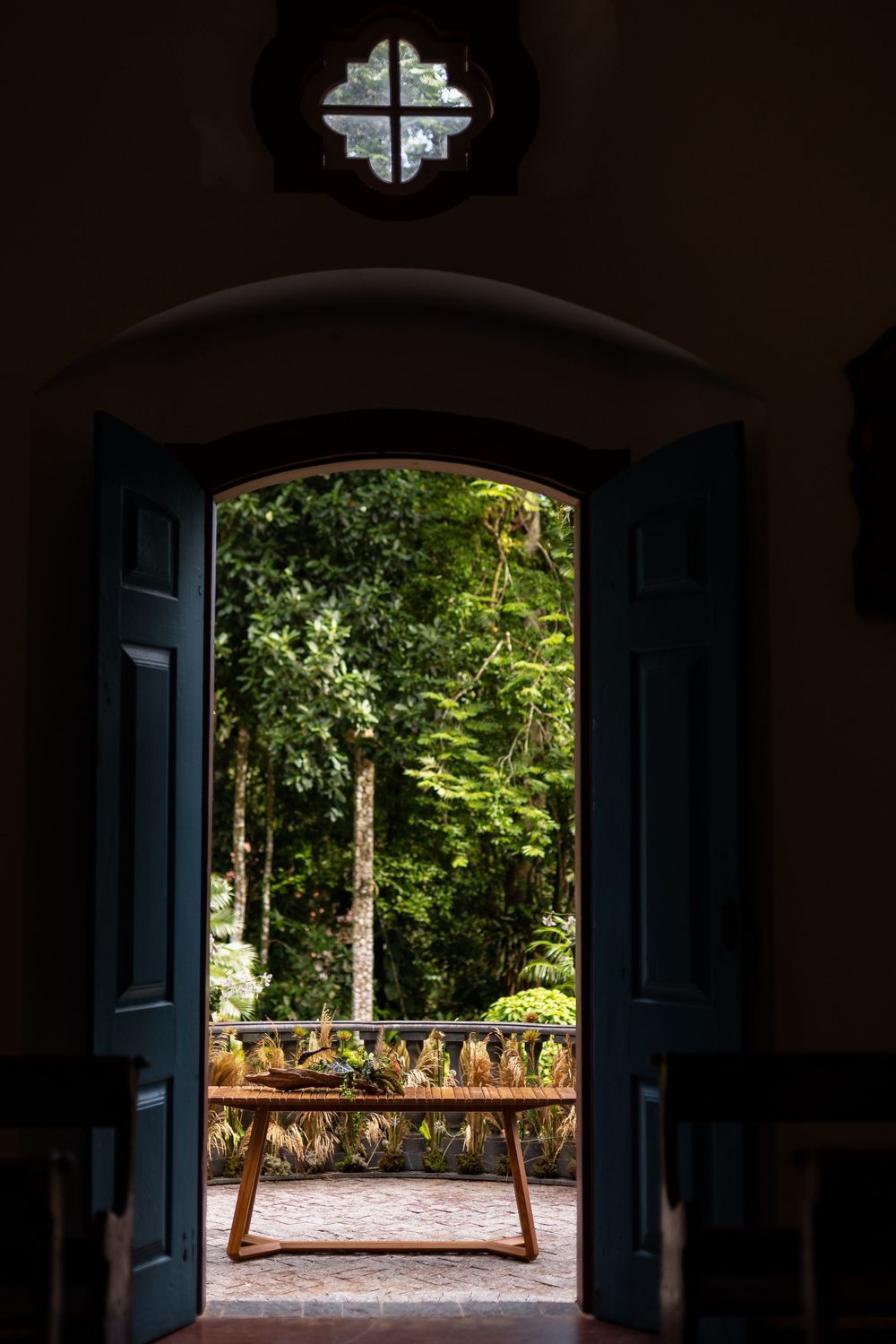 Silhouetted doorway frames a bright garden view with trees and stone railing in natural daylight.