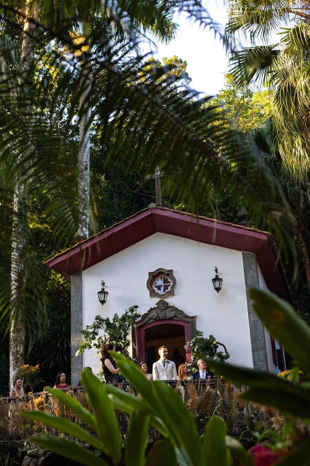White Spanish-style chapel with red trim nestled among tropical palm trees and foliage.