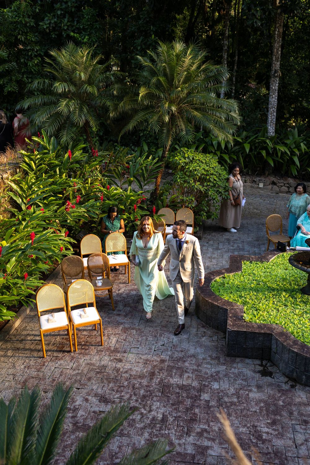 Outdoor wedding venue with elegant chairs arranged on stone patio surrounded by palm trees.