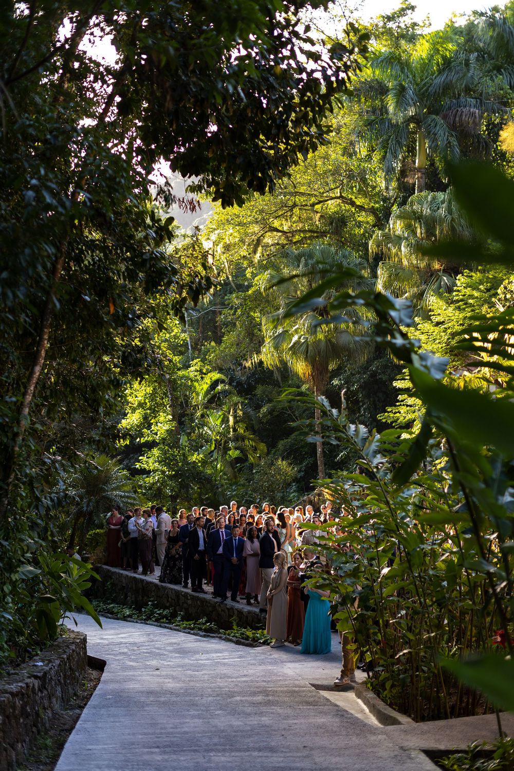 Guests line a winding garden path surrounded by lush tropical foliage and palm trees.