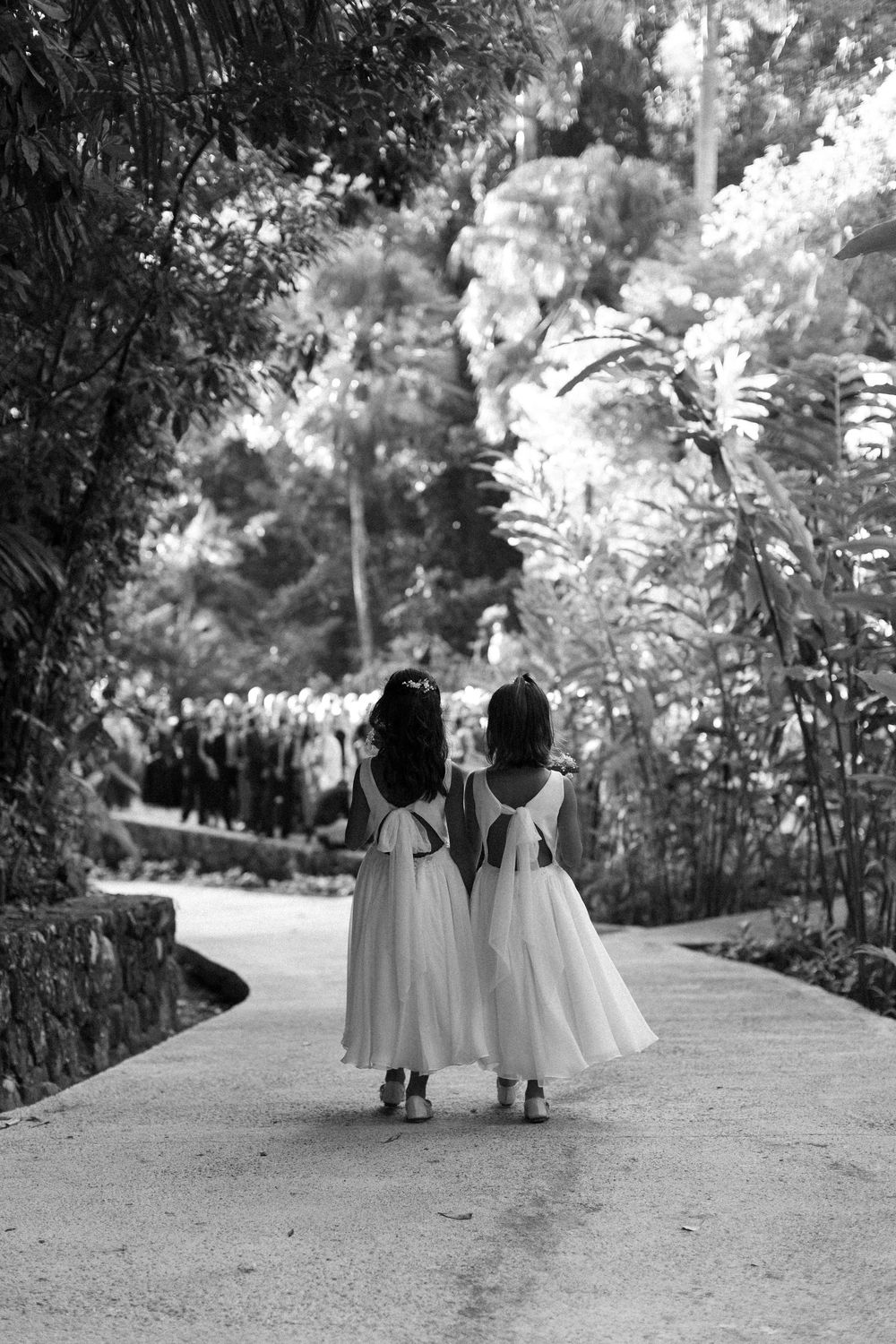 Black and white photo of wedding party members walking down a tree-lined path.