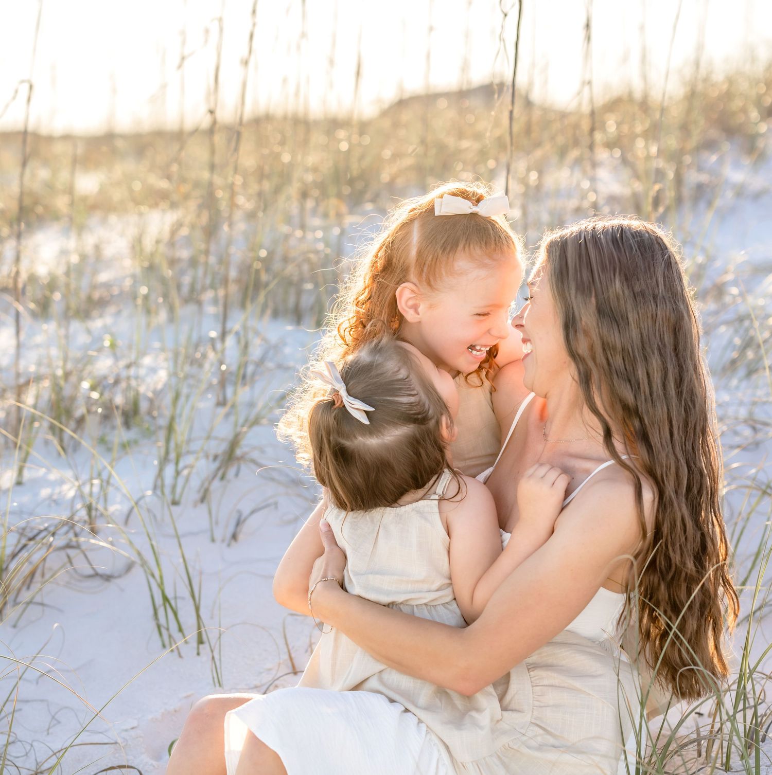 A couple shares tender moments on a sandy beach with white dunes in the background during a sunset photoshoot.