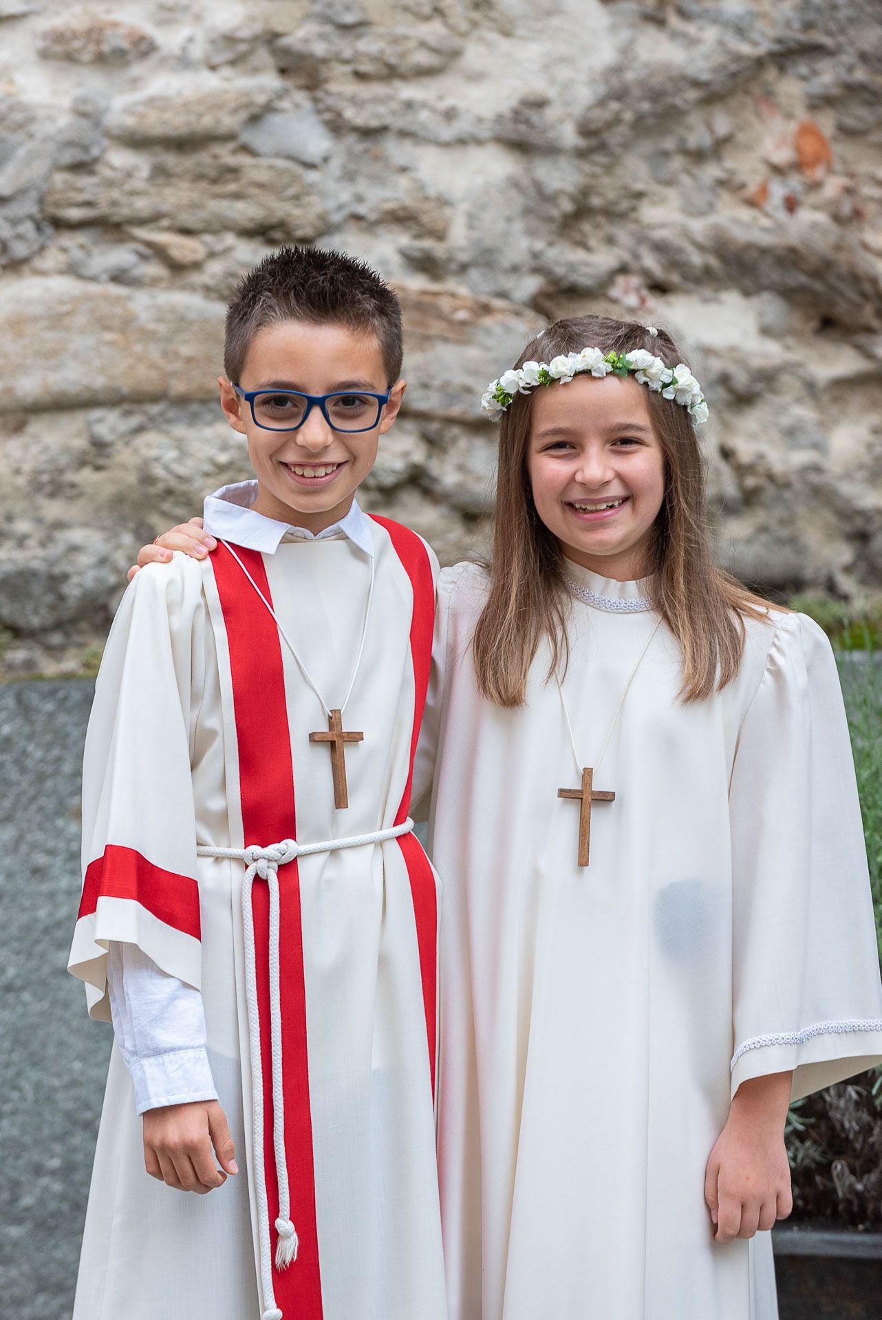 Two children in white religious ceremonial robes with crosses and floral crown.
