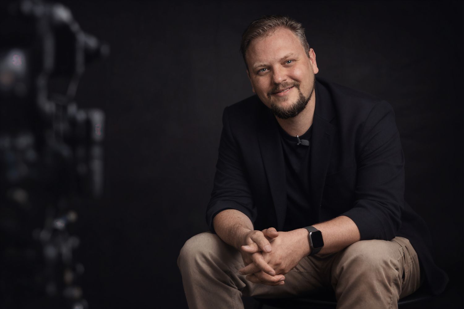Professional headshot portrait of someone in dark clothing against a black background with dramatic lighting.