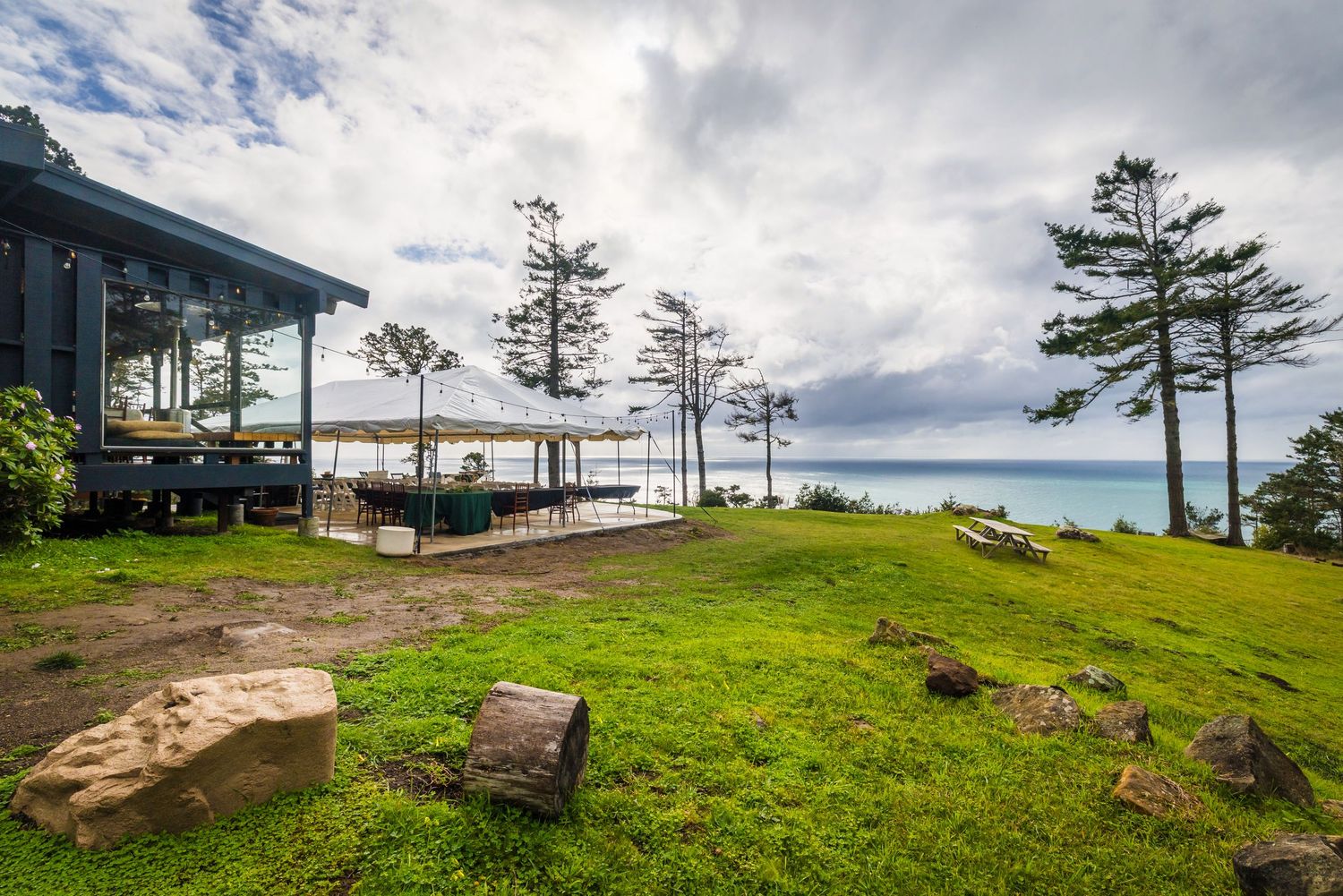 A panoramic coastal view of Norfolk Island with tall pine trees and green grass against a cloudy blue sky.