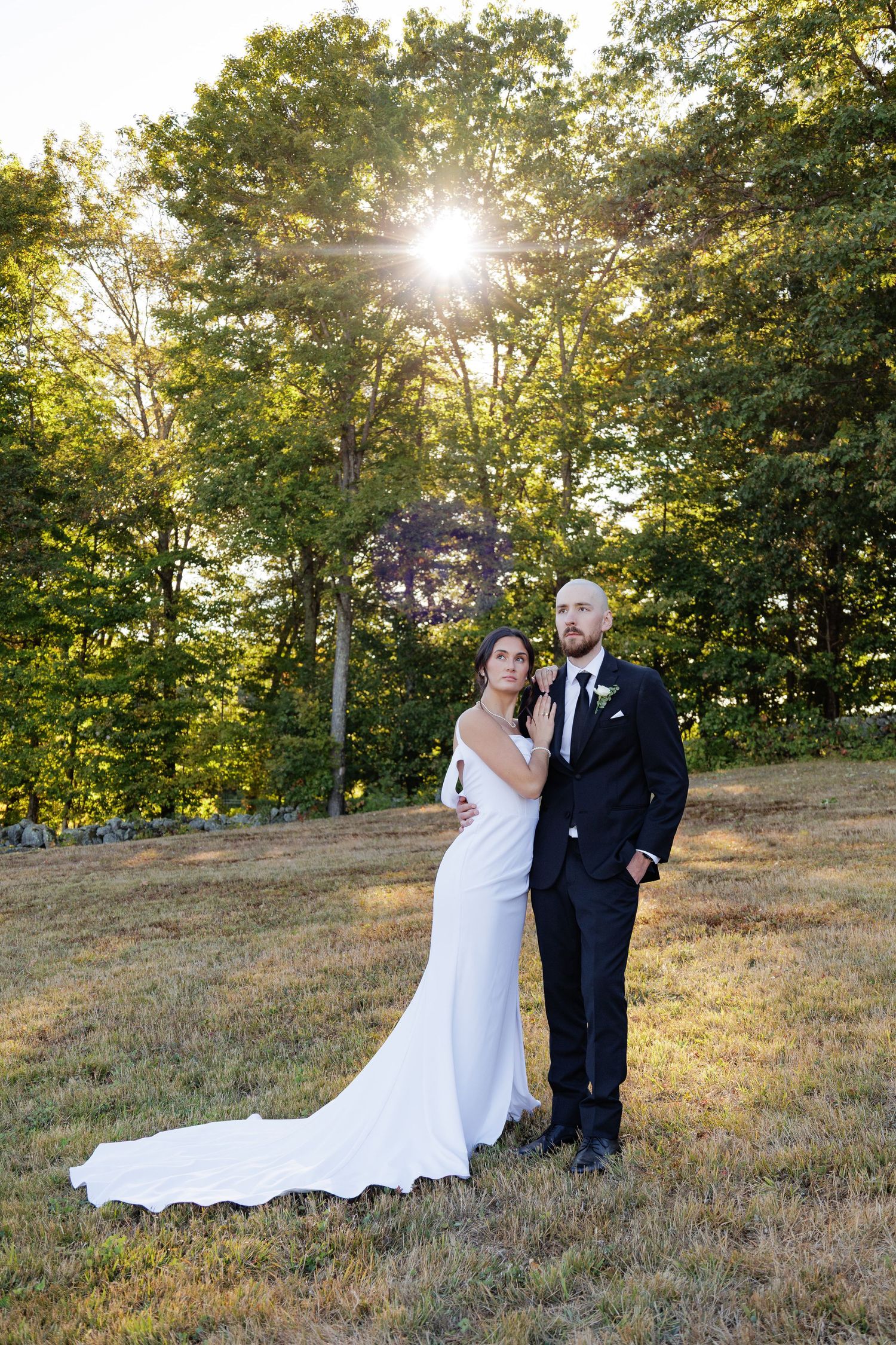 A couple shares an intimate moment on a grassy hillside at sunset with sunlight streaming through autumn trees.