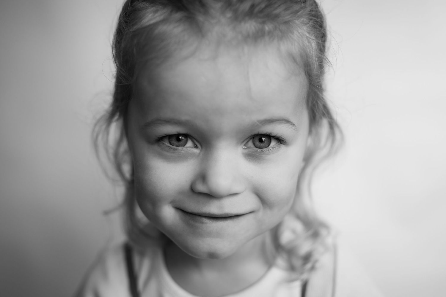 Black and white portrait of a sweet young girl with light eyes smiling softly at the camera.