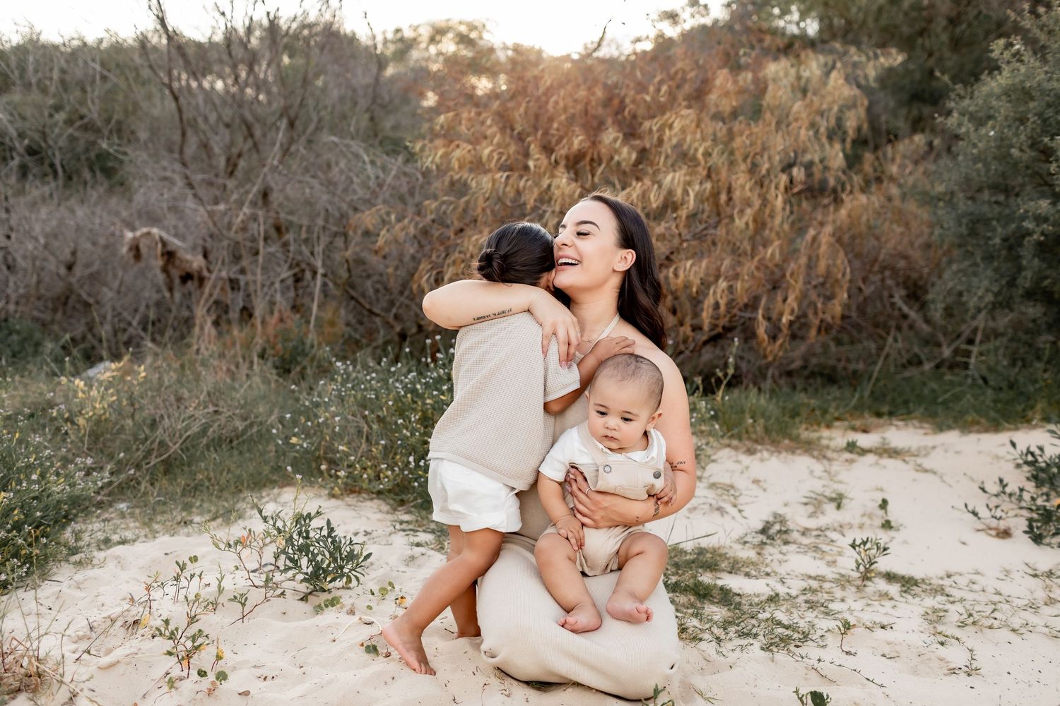 Family embraces together on sandy beach during golden hour sunset photoshoot.