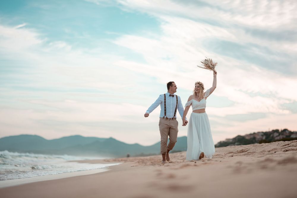 Brautpaar läuft jubelnd am weiten Sandstrand entlang. Freiheit und Freude pur bei einer Hochzeit am Meer.