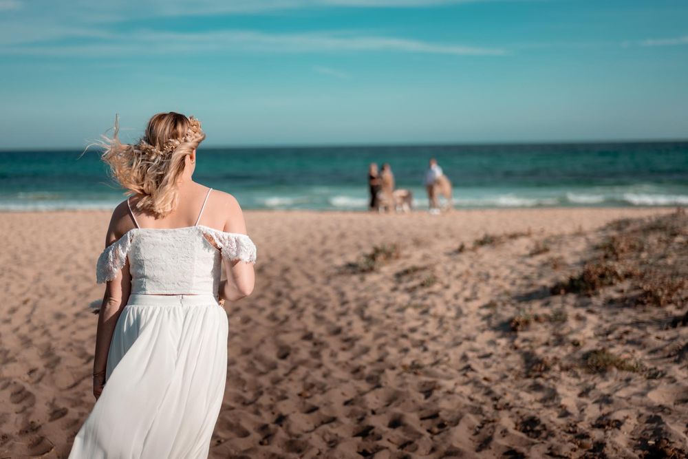 Braut blickt von hinten über den Strand auf das Meer. Ein Moment der Ruhe und Vorfreude