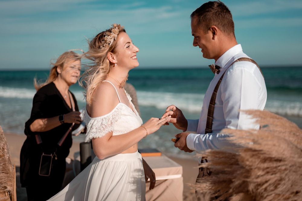 Das Brautpaar tauscht die Ringe am Strand während einer freien Trauung. Emotionale Zeremonie am Wasser.