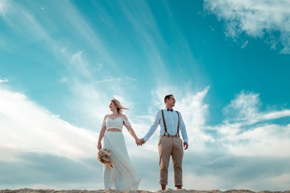 Paar steht Hand in Hand auf einer Düne vor weitem Horizont. Minimalistische und ehrliche Hochzeitsfotos.