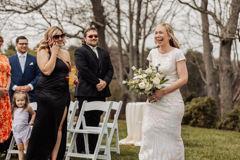 A wedding party celebrates outdoors with guests seated on white chairs during a spring ceremony.