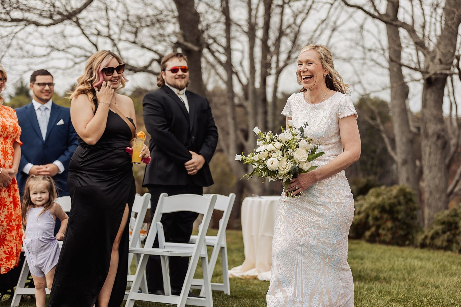 A wedding party celebrates outdoors with guests seated on white chairs during a spring ceremony.