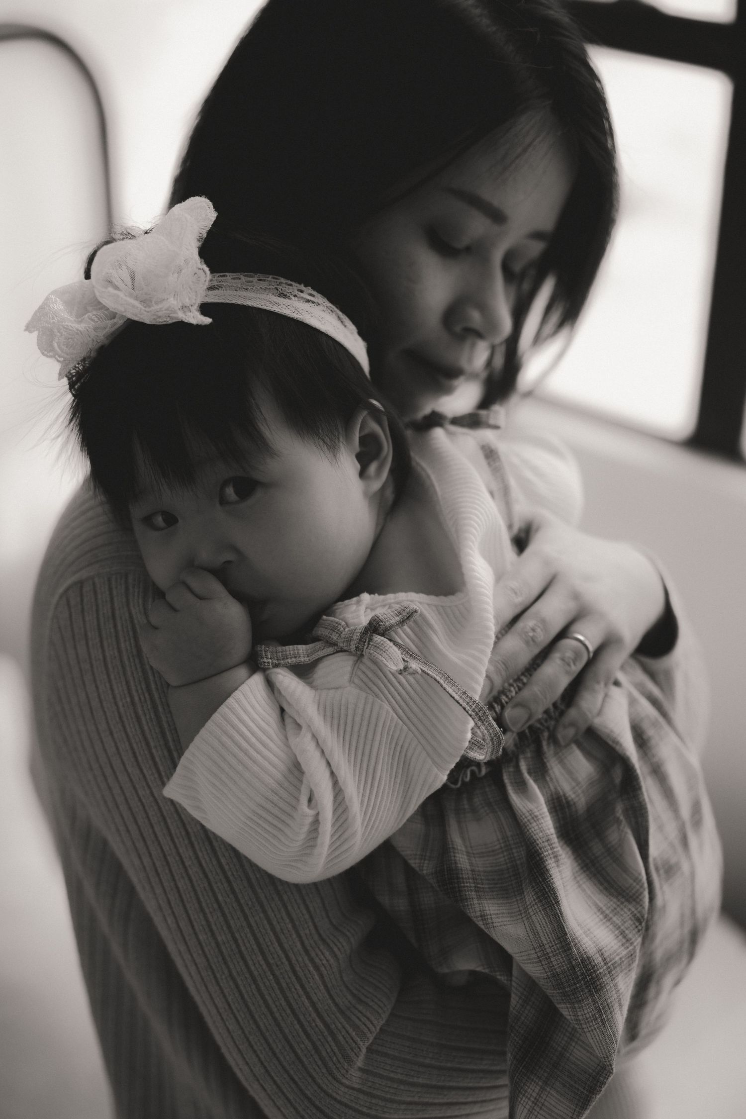 Black and white photo of an Asian mother tenderly holding her baby girl with a flower headband.一張黑白照片，照片中一位亞洲母親溫柔地抱著戴著花圈的女嬰。