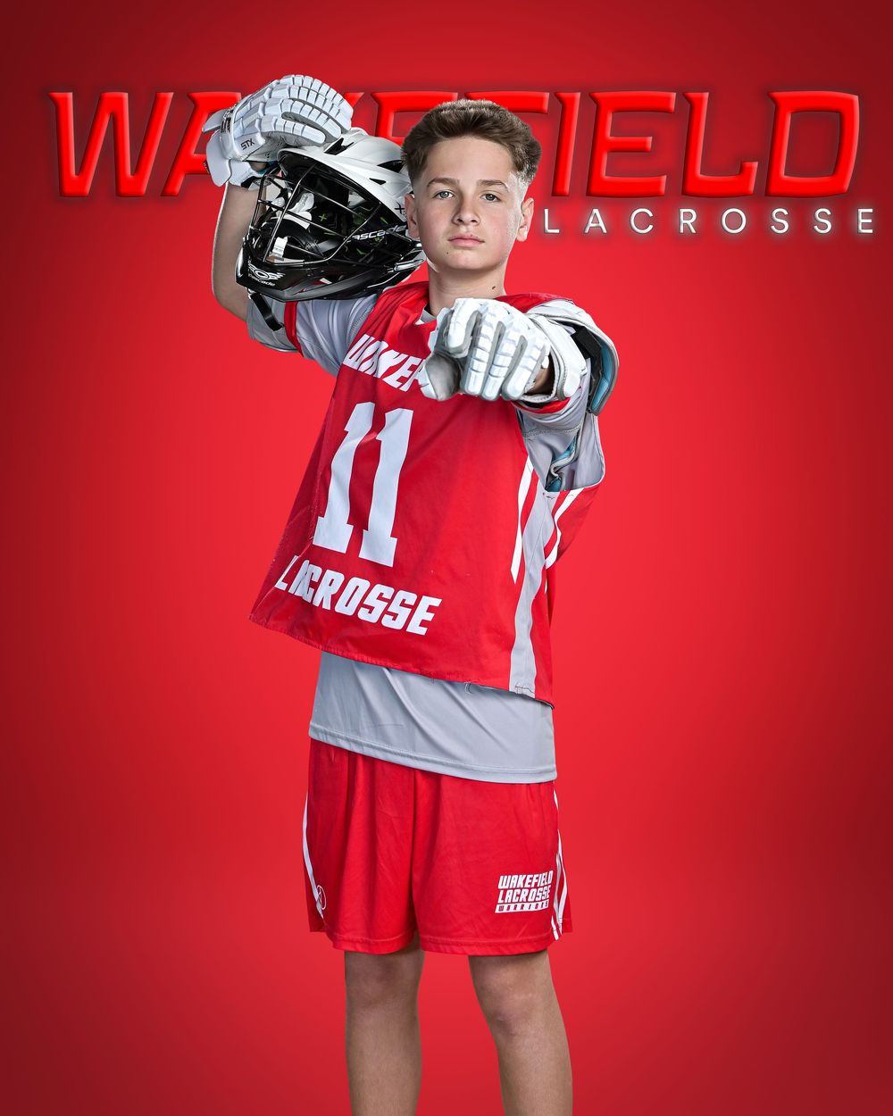 Young lacrosse player in red Wakefield Lacrosse jersey number 11, holding helmet, posed against red background.
