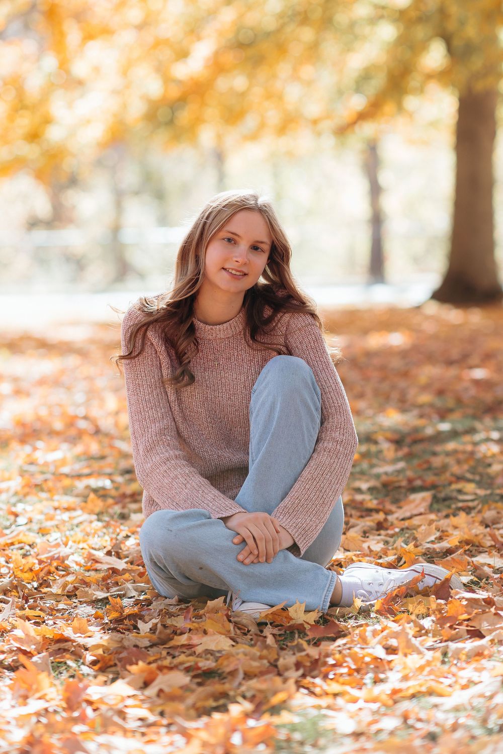 Senior girl in sweater relaxes on autumn leaves in a peaceful outdoor setting. Park senior photos. outdoor senior photos. Central Michigan