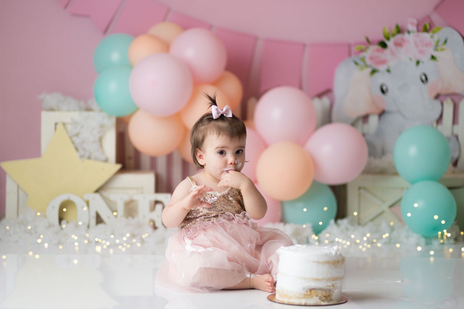 First birthday cake smash setup with pink and mint balloons, star decor, and white floral elements.