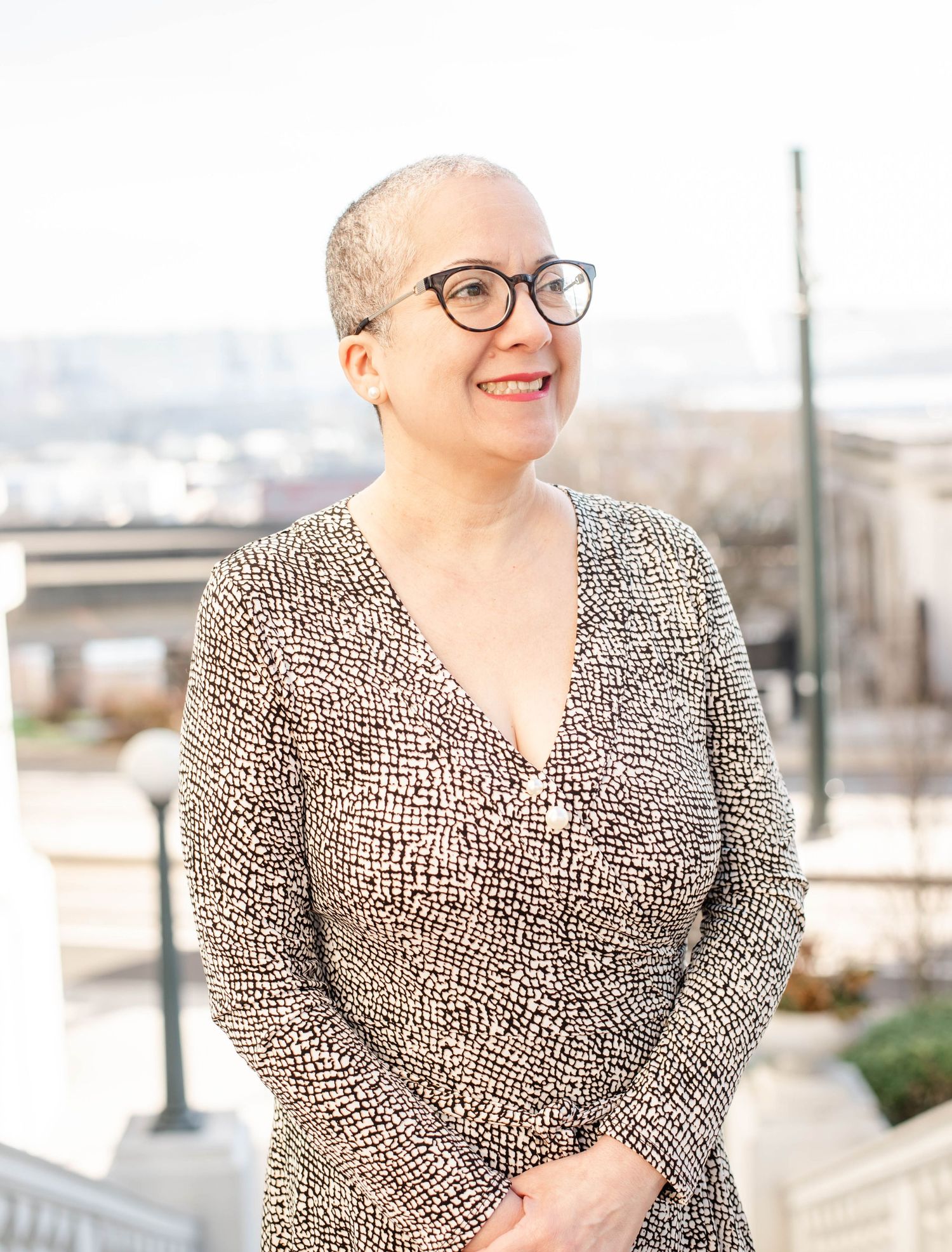 Woman in animal print dress and glasses poses cheerfully outdoors.