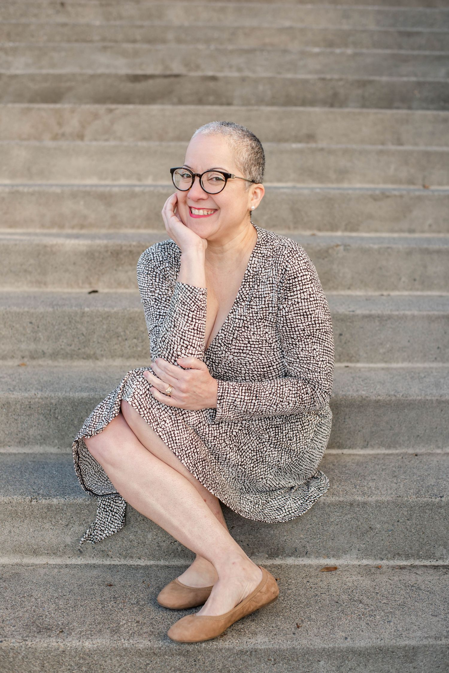 Person in patterned dress sits casually on concrete steps outdoors.