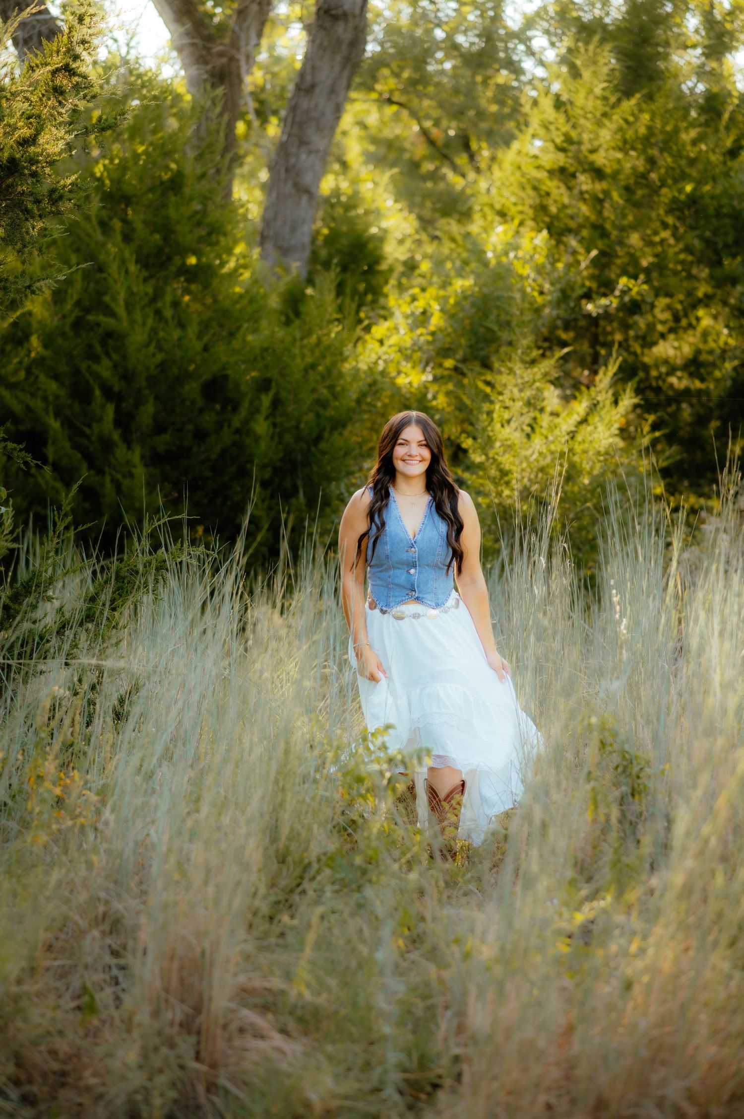 Girl walking in a green field at sunset for senior photos with an Alva OK photographer.