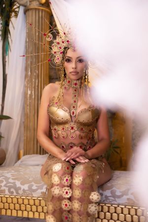 Ornate gold and pink costume with floral headdress in ethereal setting with classical columns.