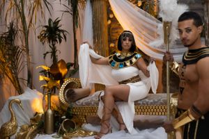 An Egyptian-themed photoshoot set with decorative columns, white drapes, and warm ambient lighting.