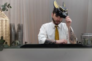 Bartender in white shirt and yellow tie wearing an Egyptian-style mask while mixing drinks.