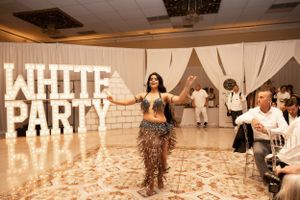 Dance performance at white-themed party with illuminated signage in background.