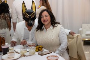 Dinner guests at an elegant event with one wearing a unique black and gold masquerade mask.