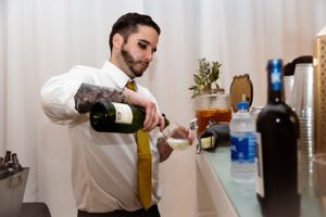 Bartender in white shirt pouring wine at an elegant event bar setup.
