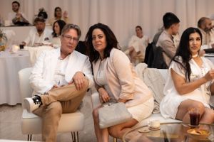 Guests in white and neutral attire seated at elegant event with modern decor.