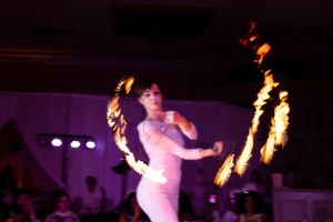 Fire dancer creates dramatic patterns with flaming props during a nighttime indoor performance.