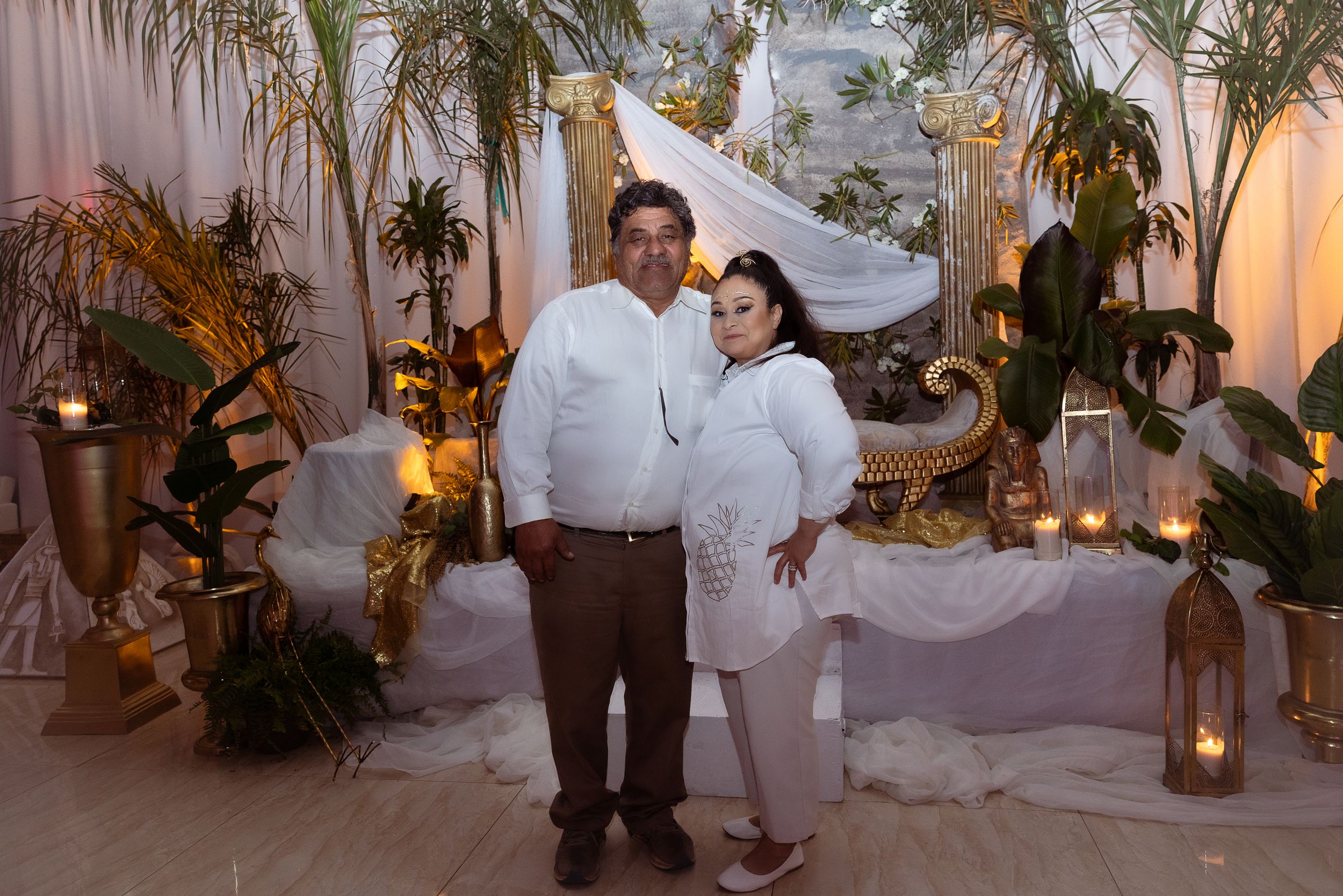 Couple posing in front of tropical themed backdrop with palm fronds and lanterns.