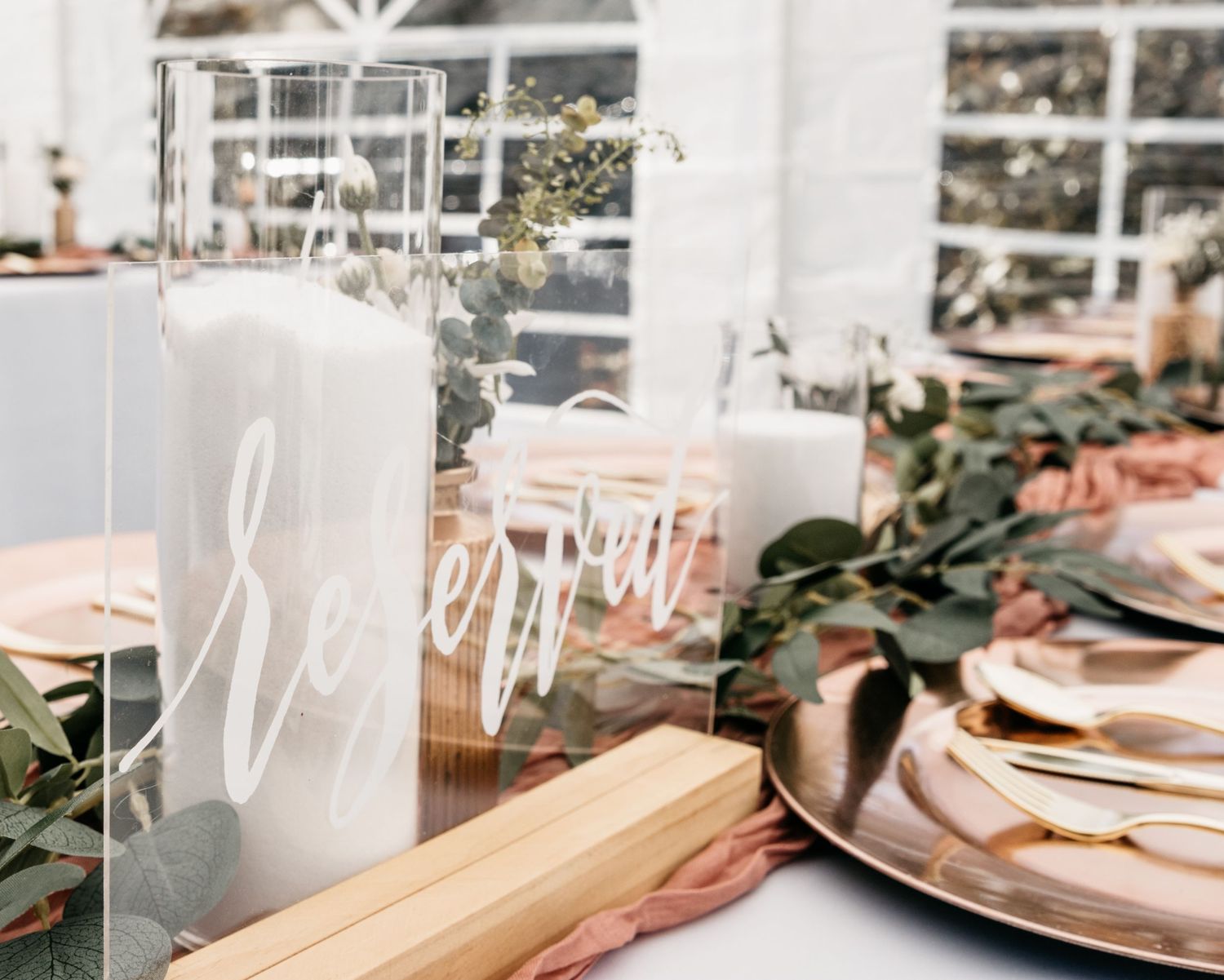Elegant wedding table setting with rose gold accents, white candles, and fresh greenery on display.