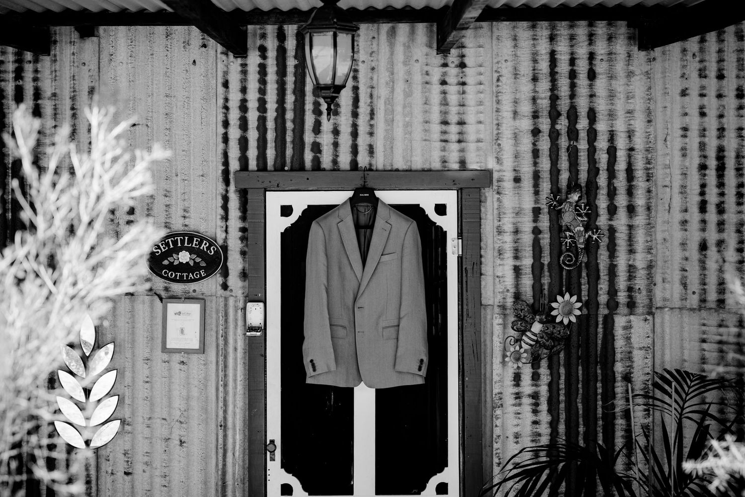 Black and white image of suit jacket displayed on screen door with corrugated metal wall background.