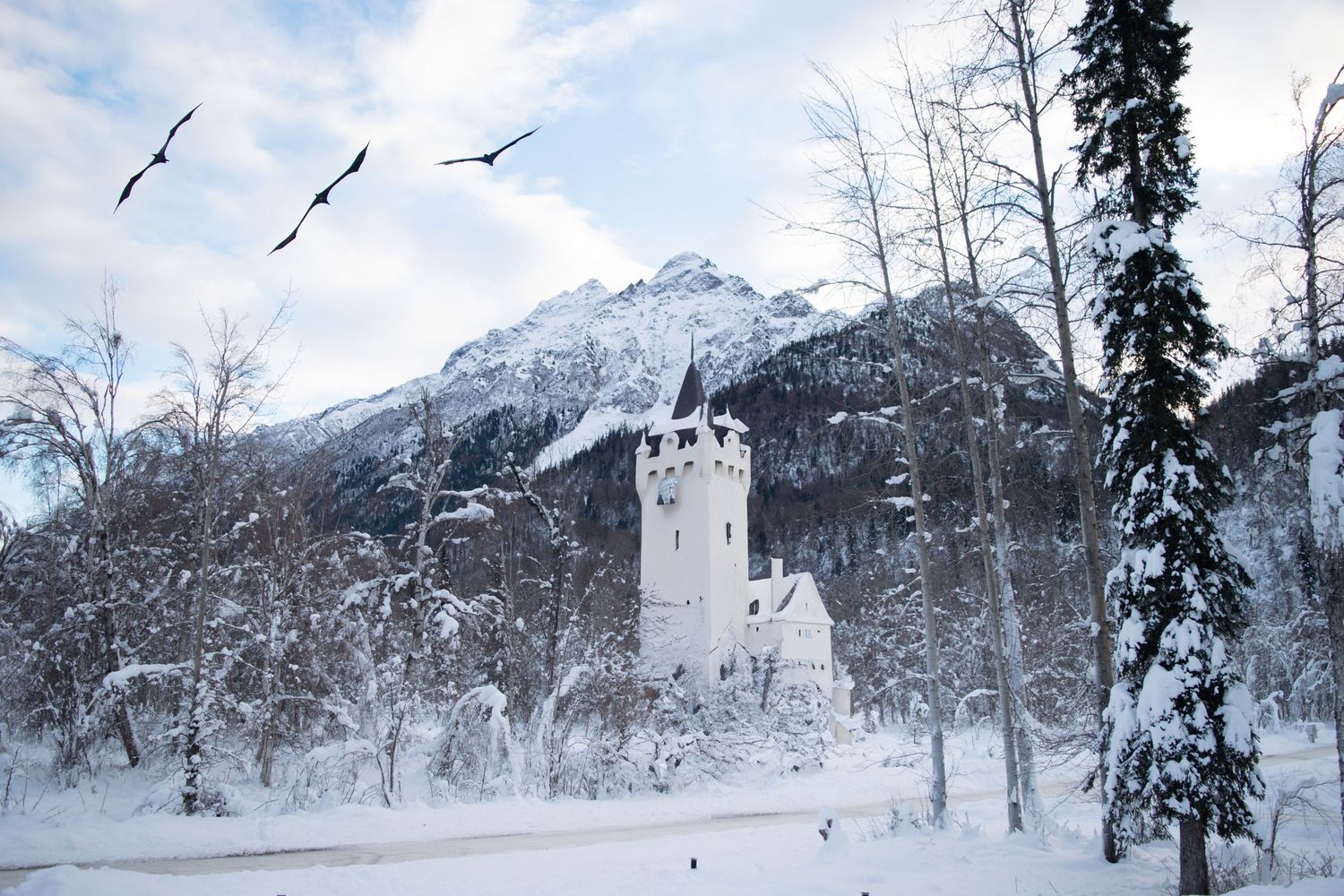A photo shopped picture of Alaskan scenery with a white castle and three dragons flying in the distance.
