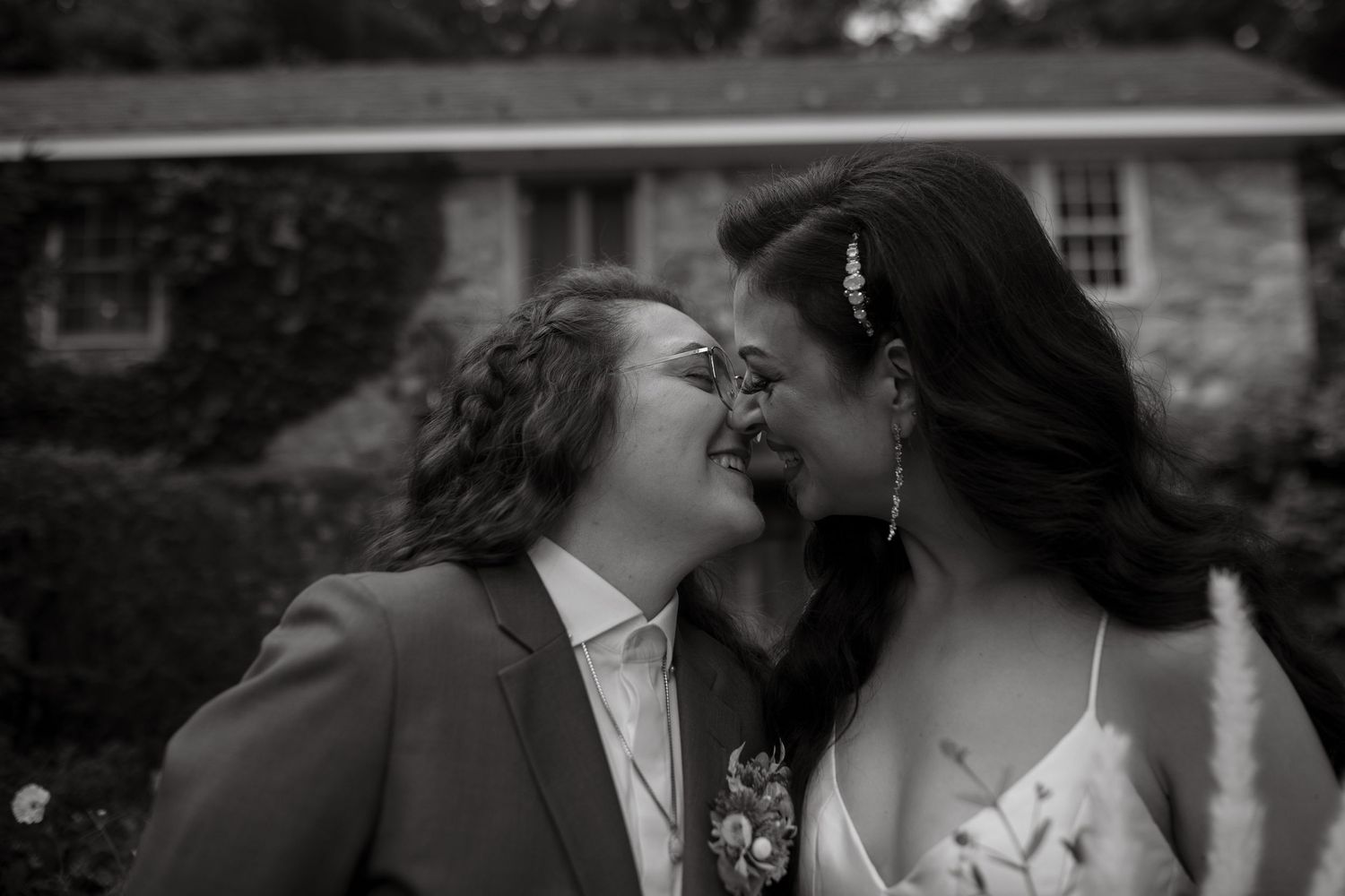A romantic black and white wedding photo of newlyweds sharing an intimate moment outdoors.