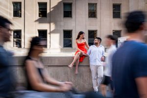 A couple shares a moment on a stone wall while crowds move past in an urban setting.