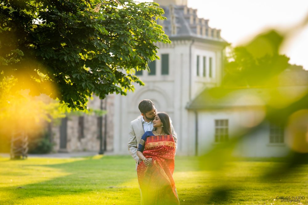 A couple embraces in a romantic golden sunset on a grassy hill near a grand historic building.