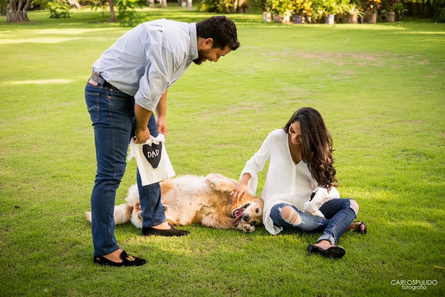 A couple plays with their golden retriever dog on a sunny lawn.