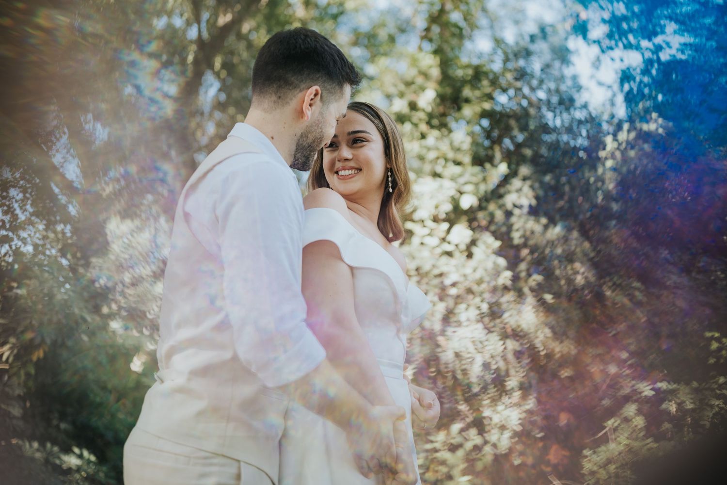 Sunlit outdoor portrait of a couple sharing an intimate moment in casual white attire.