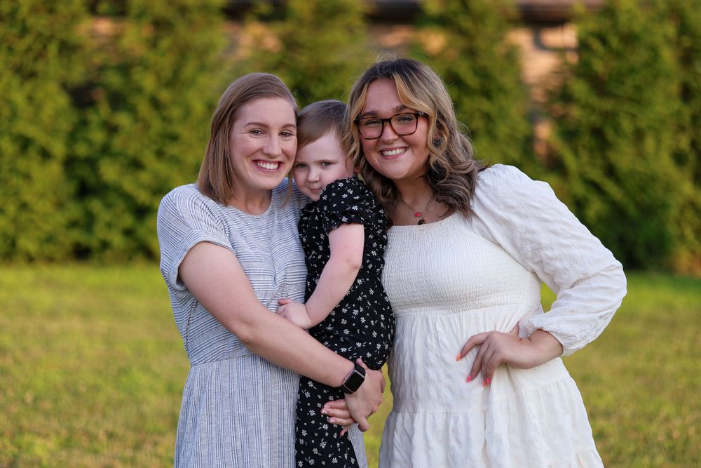 Three people pose together while enjoying golden hour in backyard setting.