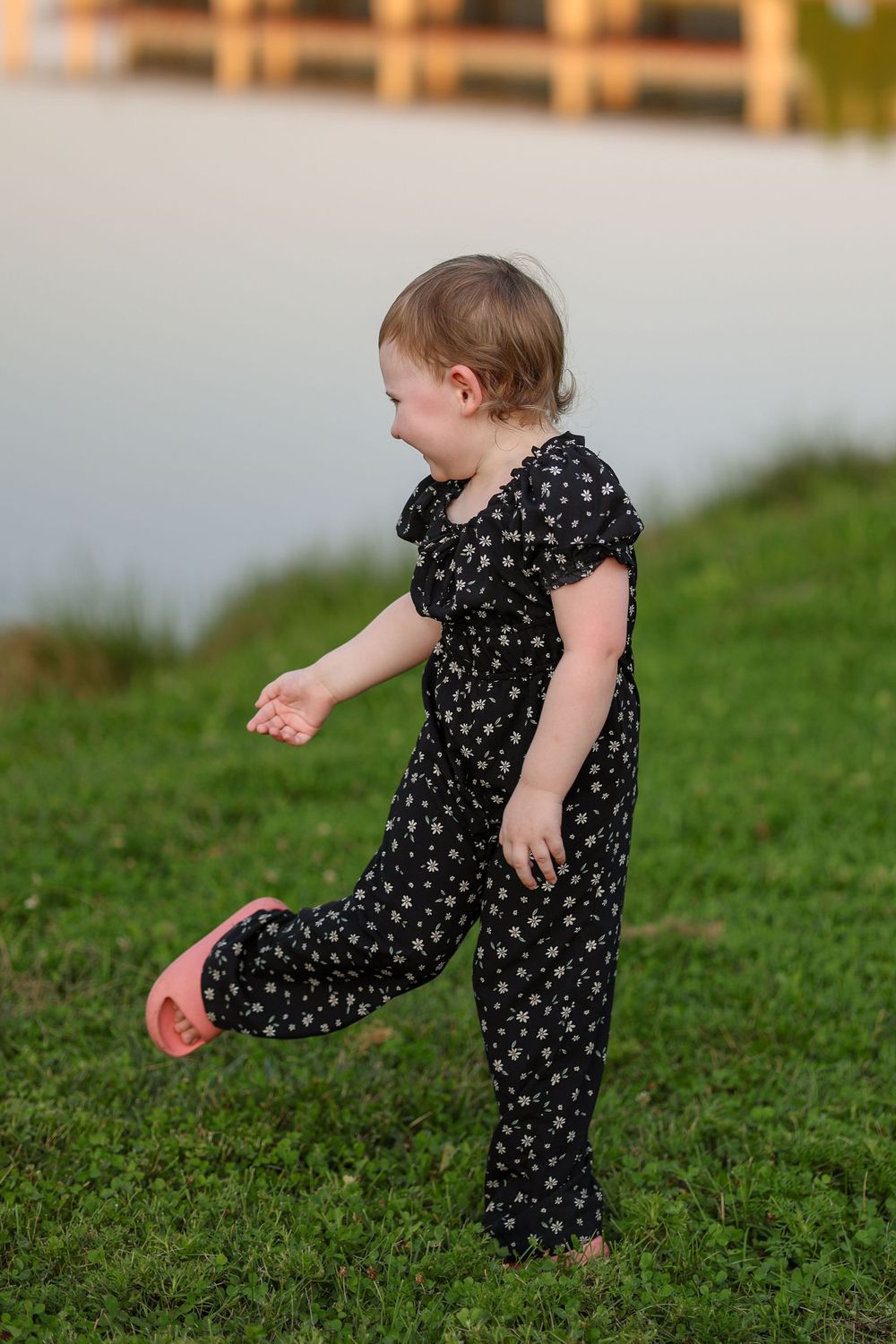 Small child in polka dot jumpsuit plays on grassy slope at dusk.