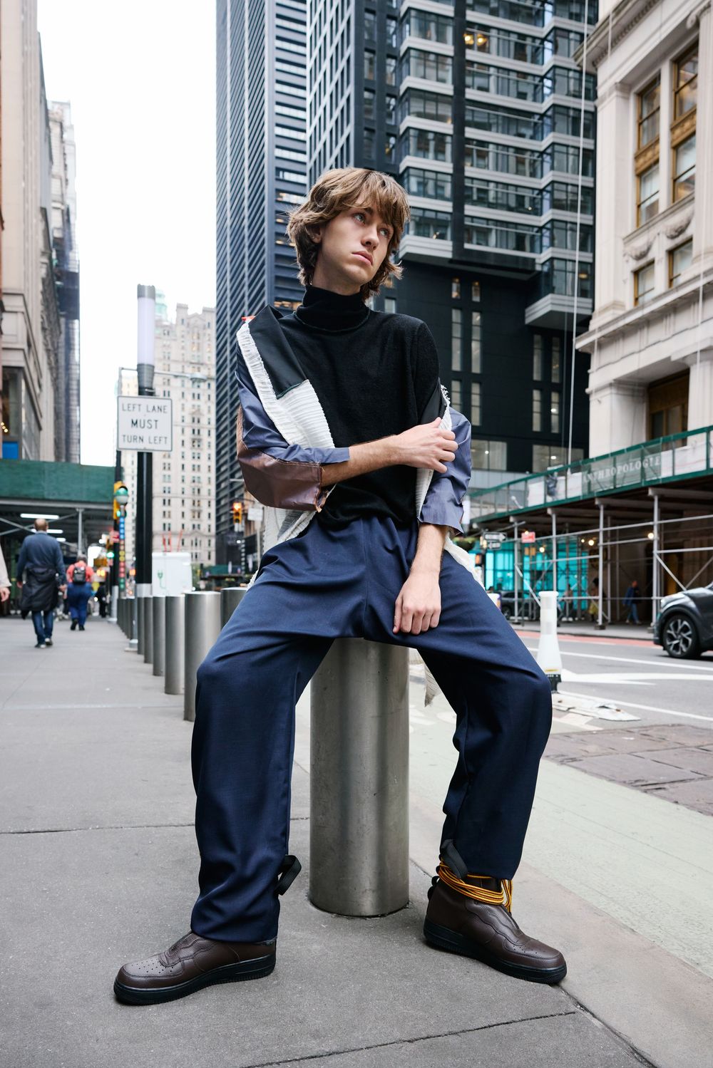 Street style fashion portrait of someone in navy workwear pants and black top posing against metal bollard in NYC.