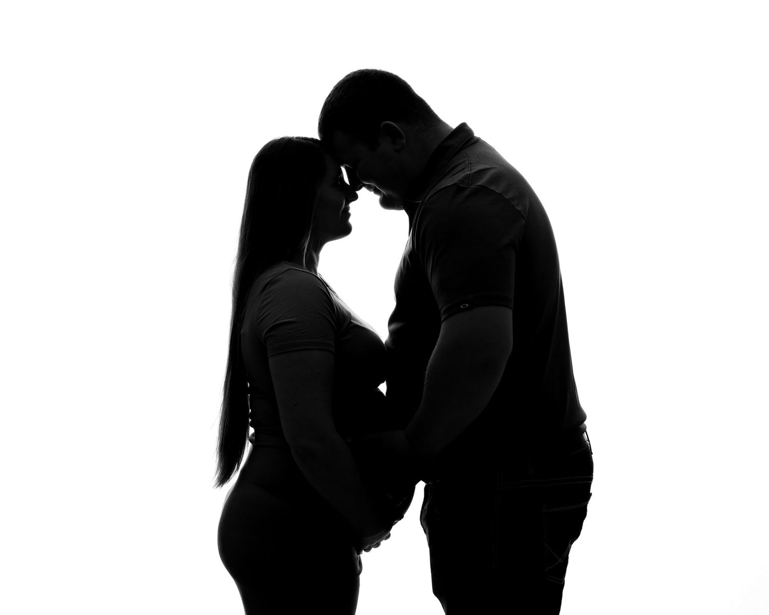 A romantic silhouette of a pregnant couple leaning in for a kiss against a white background.